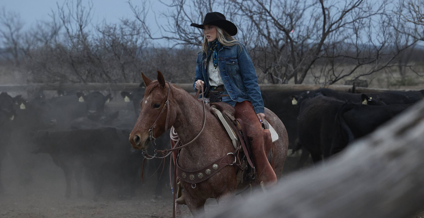 A woman wearing a black cowboy hat while riding a horse 